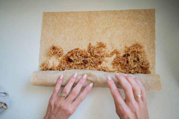 Top view of female hand rolling a delicious apple strudel dessert on a home kitchen counter. - Photo, Image