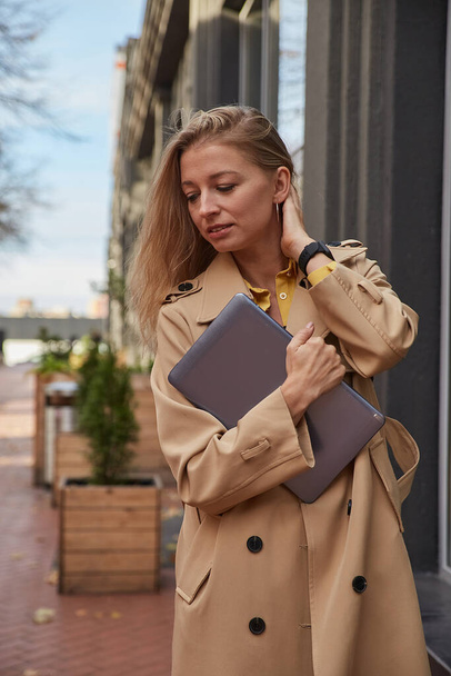 jovem caucasiano mulher no casaco segurando tablet, laptop ou ebook em mãos ao ar livre - Foto, Imagem