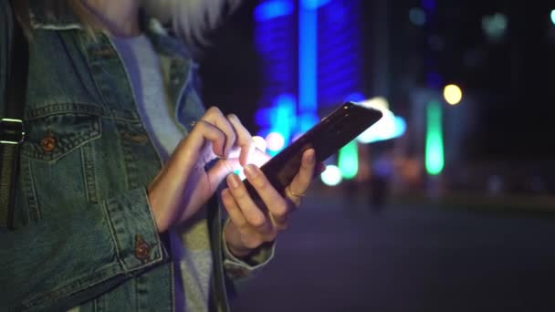 žena používá smartphone ke komunikaci v nočním městě. na pozadí mrakodrapů - Záběry, video