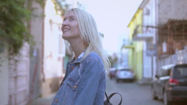 Zadní pohled na mladé stylové blondýny v džínové bundě procházky centrem města - Záběry, video