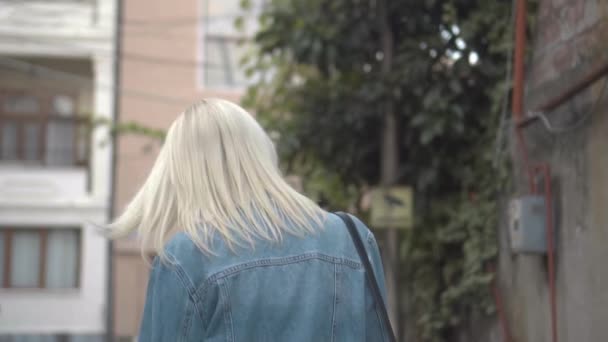 Vue arrière de la jeune blonde élégante veste en denim marchant à travers le centre-ville - Séquence, vidéo