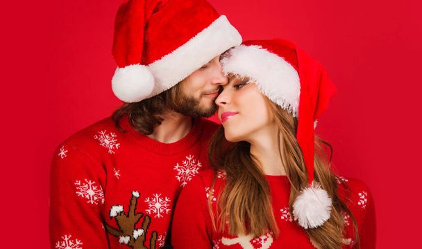 クリスマスのセーターとサンタの帽子の若いカップル。新年の広告。メリークリスマス。関係概念. - 写真・画像