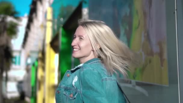 Vue arrière de la jeune blonde élégante veste en denim marchant à travers le centre-ville - Séquence, vidéo