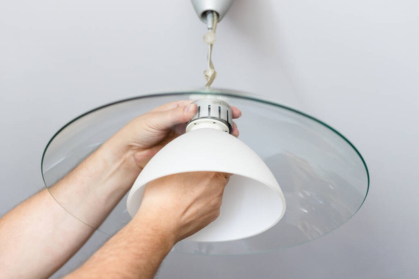 man monteert lampenkap van plafondlamp thuis - Foto, afbeelding