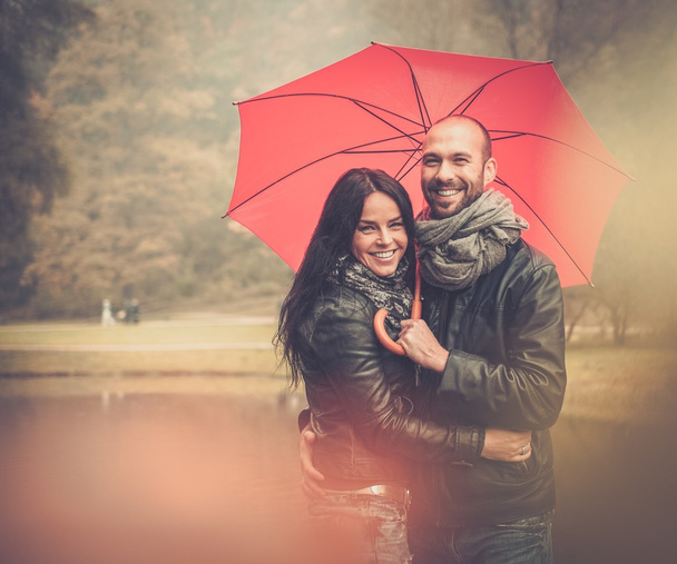 glückliches Paar mittleren Alters mit Sonnenschirm im Freien an einem schönen regnerischen Herbsttag   - Foto, Bild