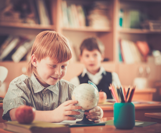 Little redhead schoolboy behind school desk during lesson  - Фото, изображение