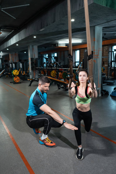 young female exercising and has workout with trx and personal trainer in gym - Foto, Imagem