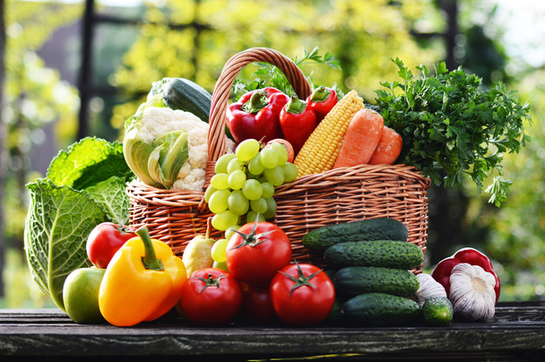 Плетеная корзина с различными сырыми органическими овощами в саду
 - Фото, изображение