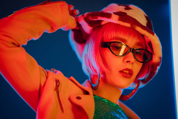 Portrait of glamorous woman on party under glowing neon light. Nightclub, trendy outfit. Teenager, zoomer Z-generation. Lady in hat and glasses.  - Foto, Imagem