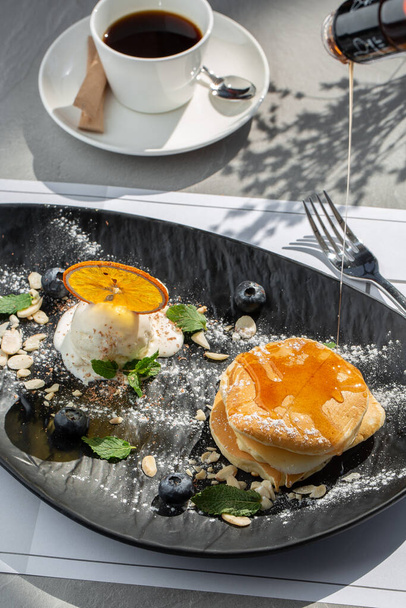 Amerikanische Pfannkuchen mit Eiskugel, Beeren und Ahornsirup auf schwarzem Teller, isoliert mit Kaffee. Café-Speisekarte - Foto, Bild