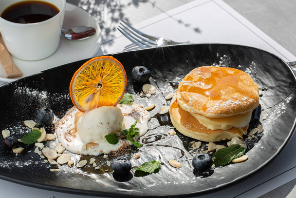 American pancakes with ice cream scoop, berries and maple syrup on black plate isolated with coffee. cafe menu - Foto, imagen