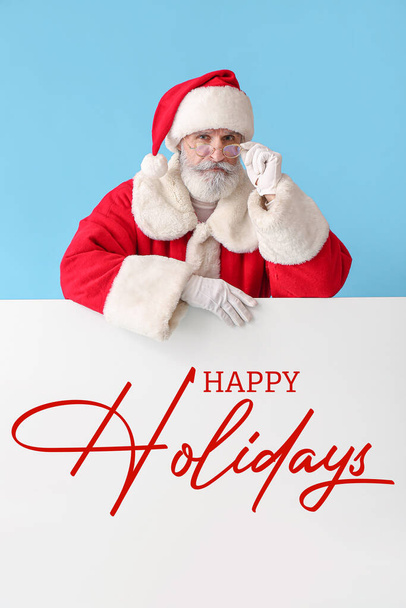 Santa Claus with poster on color background. Happy holidays - Фото, изображение