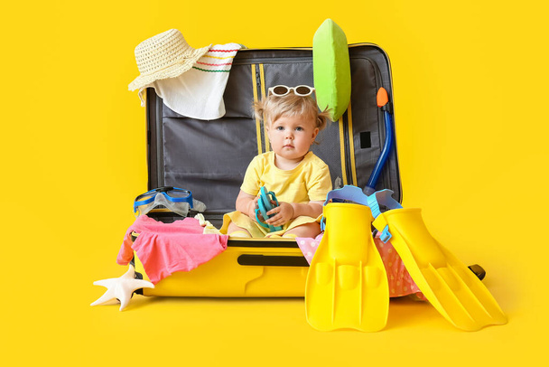 Nettes Baby Mädchen im Koffer mit Habseligkeiten auf farbigem Hintergrund - Foto, Bild