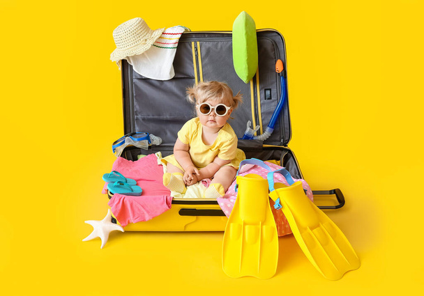Cute baby girl in suitcase with belongings on color background - Foto, immagini