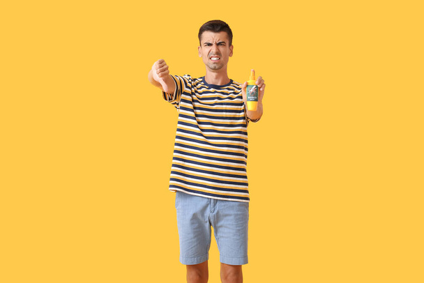 Displeased young man with mosquito repellent showing thumb-down on color background - Foto, imagen