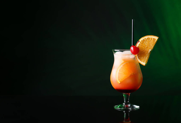 Glass of tasty Tequila Sunrise cocktail on dark color background - Photo, Image