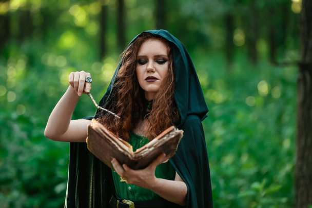 Young witch with spell book in green forest - 写真・画像