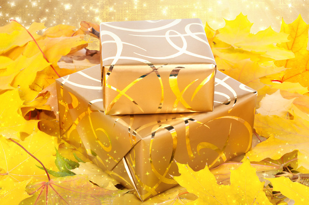 Gift box in gold wrapping paper with autumn leaves on the abstra - Foto, immagini