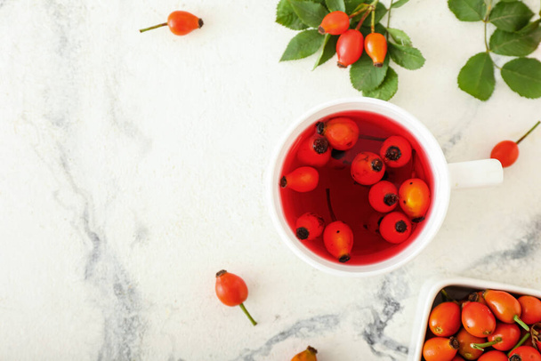 Cup of tasty rose hip tea and berries on white marble background - Photo, Image