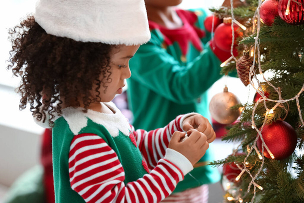Kis afro-amerikai lány öltözött elf díszítő karácsonyfa otthon - Fotó, kép