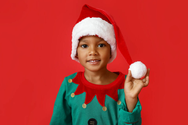 Kleine Afro-Amerikaanse jongen in Santa hoed op rode achtergrond - Foto, afbeelding