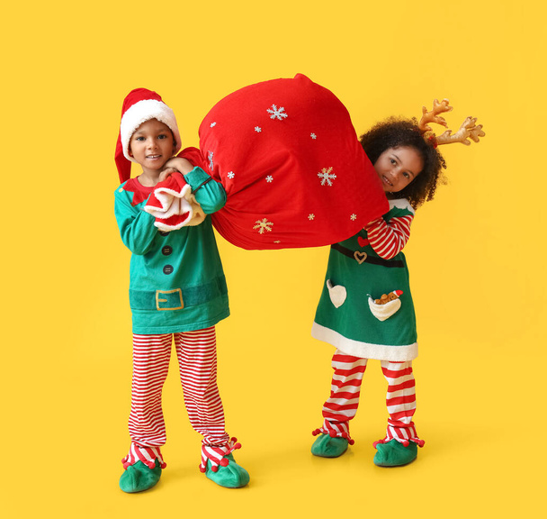 Lindos pequeños elfos sosteniendo la bolsa de Santa sobre fondo amarillo - Foto, Imagen