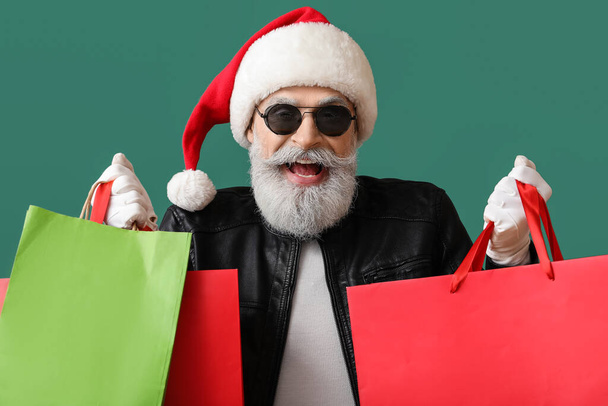 Cool Kerstman in lederen jas en met boodschappentassen op kleur achtergrond - Foto, afbeelding