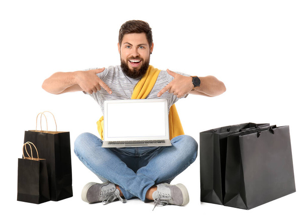 Handsome man with Black Friday shopping bags pointing at laptop on white background - Photo, Image