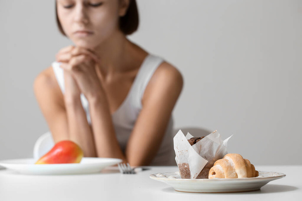 Mladá žena u stolu na šedém pozadí, soustřeďte se na jídlo. Anorexie koncept - Fotografie, Obrázek