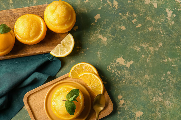 Bord met lekkere ijsjes in sinaasappelschillen op grunge kleur achtergrond - Foto, afbeelding