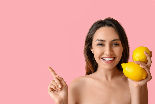 Голая молодая женщина со свежими лимонами показывает что-то на цветном фоне. День вегана - Фото, изображение