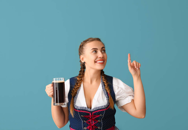 Молодая официантка с пивом, указывающая на что-то на синем фоне - Фото, изображение