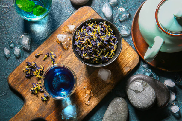 Copo de chá azul orgânico, flores secas e cubos de gelo em fundo escuro - Foto, Imagem