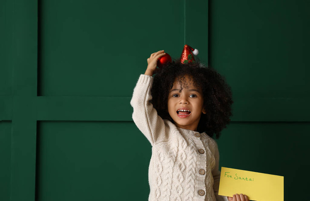 Cute African-American girl with letter to Santa on color background - Фото, зображення