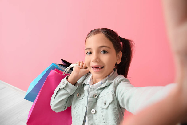 Little girl with Black Friday shopping bags taking selfie near pink wall - Fotó, kép