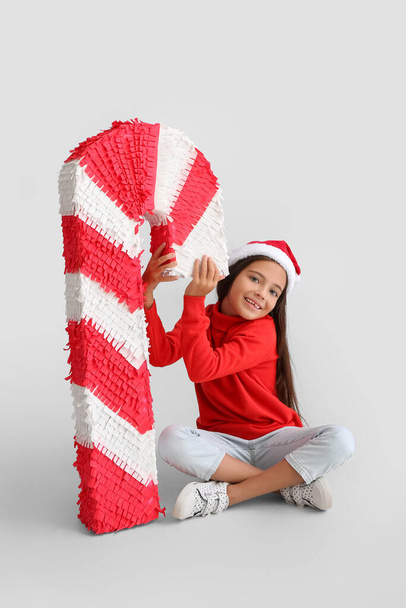 Klein meisje in Santa hoed en met snoep stok pinata op lichte achtergrond - Foto, afbeelding