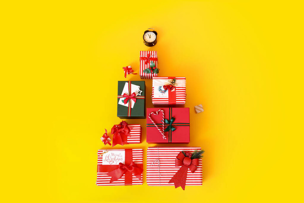 Christmas tree made of gift boxes and alarm clock on yellow background - Photo, Image