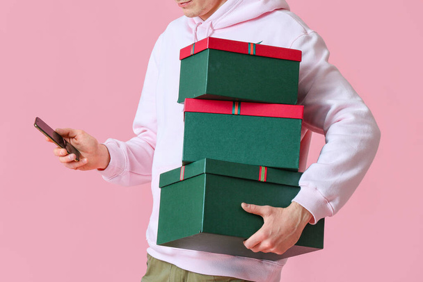 Człowiek z pudełkami na prezenty świąteczne za pomocą telefonu komórkowego na różowym tle - Zdjęcie, obraz