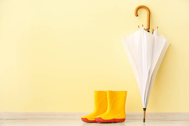 Paar gele rubberen laarzen en paraplu op de vloer in de buurt van kleur muur - Foto, afbeelding