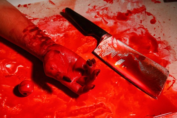 Afgesneden hand en hakmes op tafel met bloedvlekken - Foto, afbeelding