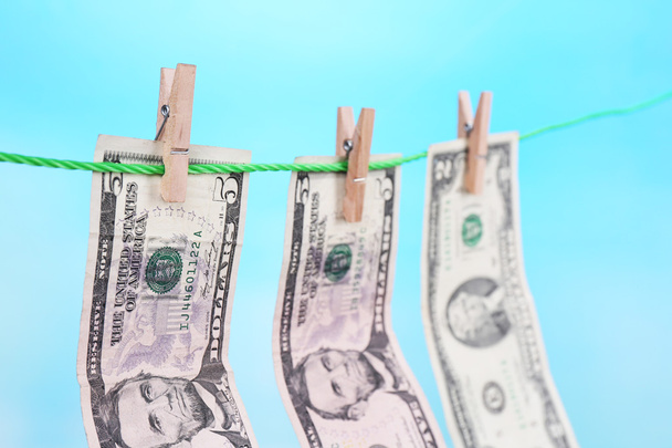 Dollar bills hanging on rope attached with clothes pins. Money-laundering concept. On bright background. - Foto, immagini