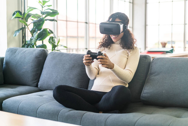 Mujer latina usando un auricular de realidad virtual en el sofá en casa - Foto, imagen