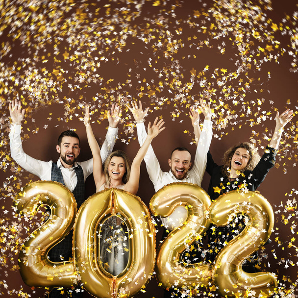 Group of party people celebrating arrival of 2022 New Year with a golden balloons and falling confetti - Foto, Bild