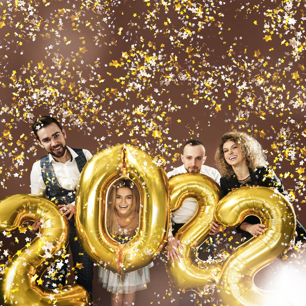 Group of party people celebrating arrival of 2022 New Year with a golden balloons and falling confetti - Photo, Image