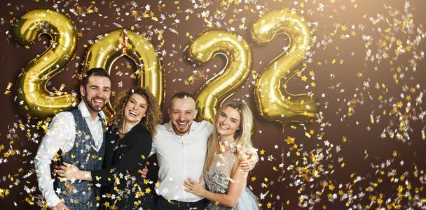 Group of party people celebrating arrival of 2022 New Year with a golden balloons and falling confetti  - Foto, imagen