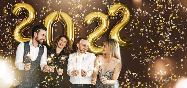 Happy party people celebrating 2022 New Year with burning sparklers and falling confetti - 写真・画像