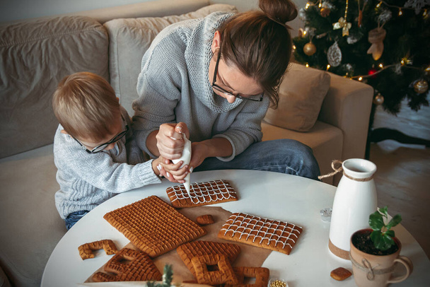A Little boy with mom decorate christmas gingerbread house together - Foto, imagen
