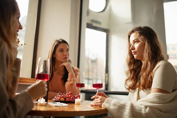 Portrait of three beautiful women sitting at cafe, talking and drinking red wine. Weekend gathering - Foto, Bild