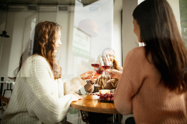 Veselí přátelé se setkávají v kavárně, jedí, pijí víno za teplého slunečného dne - Fotografie, Obrázek