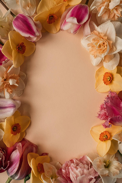 Esthetische platte lay frame met kleurrijke rozen, narcissen, tulpenbloemen en bloemblaadjes op neutrale gember achtergrond. Bovenaanzicht blanco kopieerruimte template - Foto, afbeelding